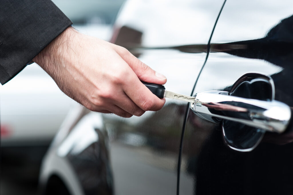 Closeup of a man's hand inserting key into the door lock of a car.